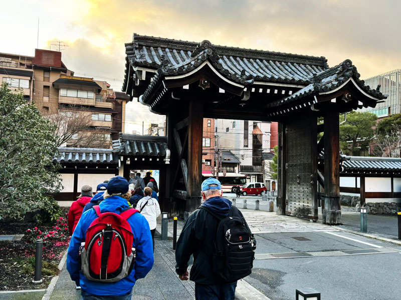 A group of people walking towards a traditional Japanese gate, with buildings in the background.