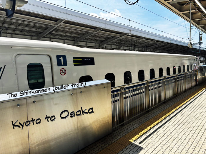 A Shinkansen bullet train at a station, with signage indicating the route from Kyoto to Osaka.