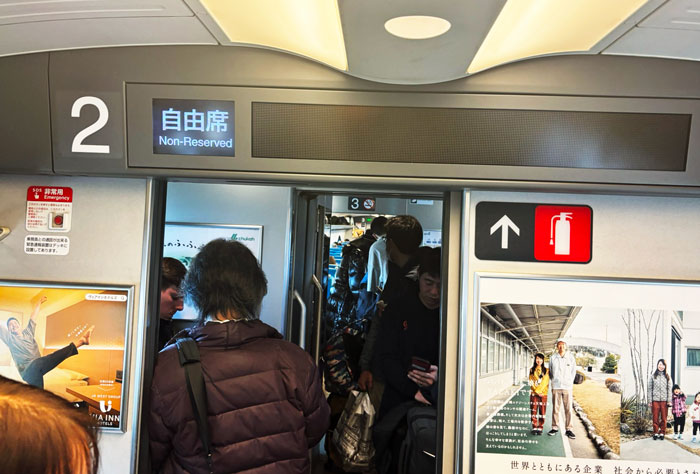 View of passengers entering a train carriage marked with a non-reserved seat sign, featuring an interior with a busy atmosphere.