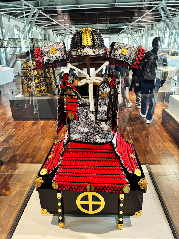 A historical samurai armor displayed in a glass case, featuring intricate patterns and vibrant red and black colors.